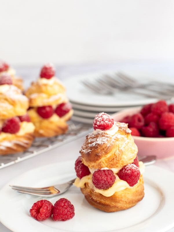 Raspberry vanilla custard profiteroles filled with vanilla custard, whipped cream and fresh raspberries, dusted with icing sugar.