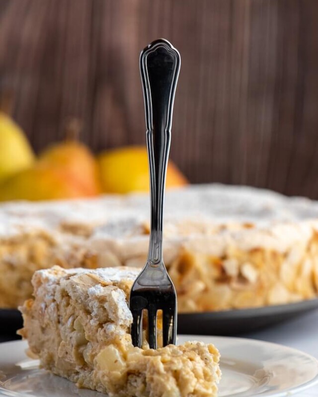 Praline pear meringue cake layered with creamy pear mousseline and almond meringue, with a slice served on a plate.