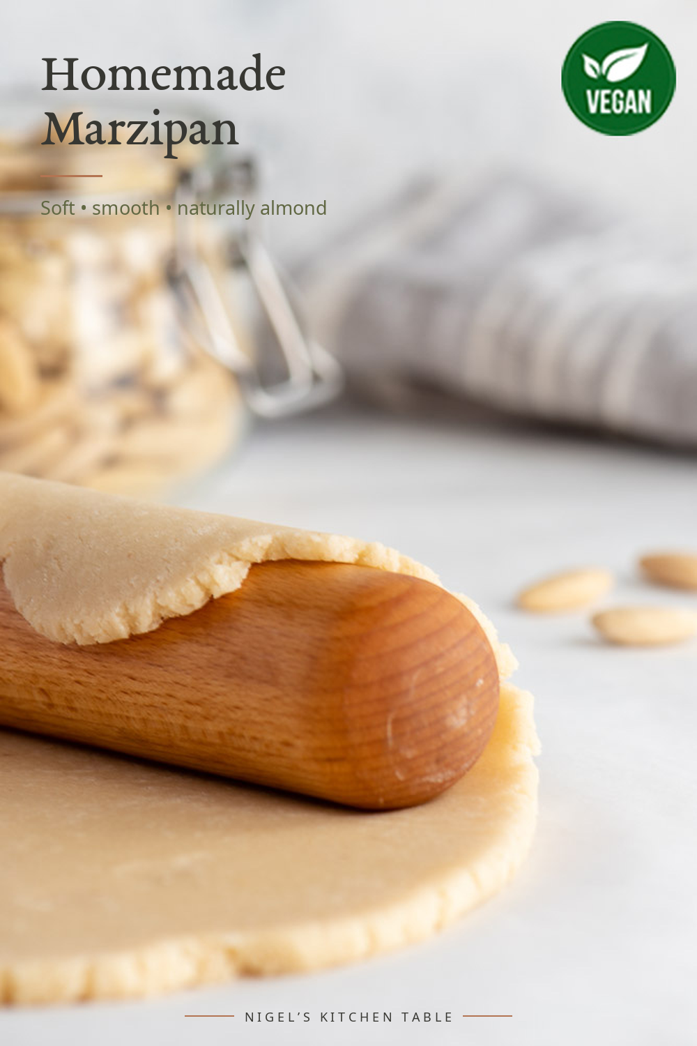 Homemade marzipan rolled into a smooth log with blanched almonds in the background.