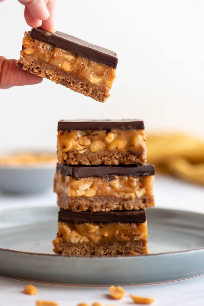 Millionaire’s Biscoff bars stacked on a plate with layers of biscuit base, peanut caramel and dark chocolate ganache.