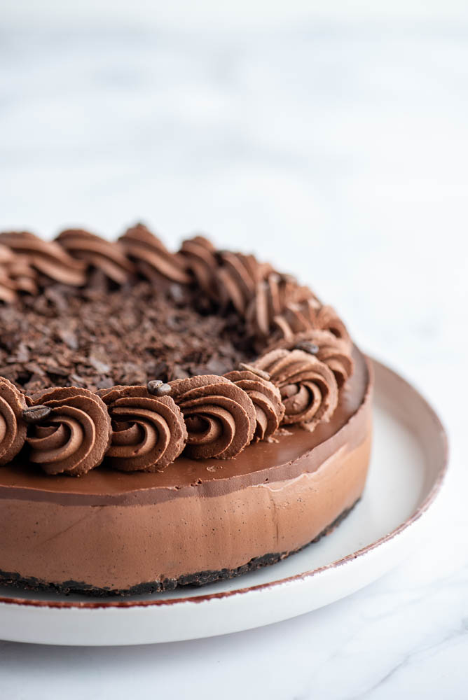 Slice of no-bake espresso chocolate cheesecake with an Oreo biscuit base, creamy chocolate filling and piped coffee ganache.